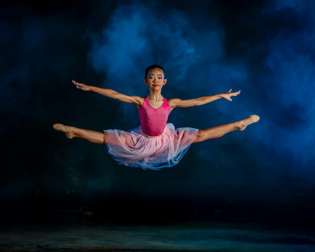 Graceful ballerina in a pink tutu executing a perfect leap against a dramatic backdrop.